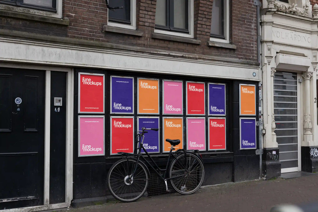 Wall with multiple colorful poster mockups by June Mockups arranged in a grid on a street in Amsterdam, with a black bicycle parked in front