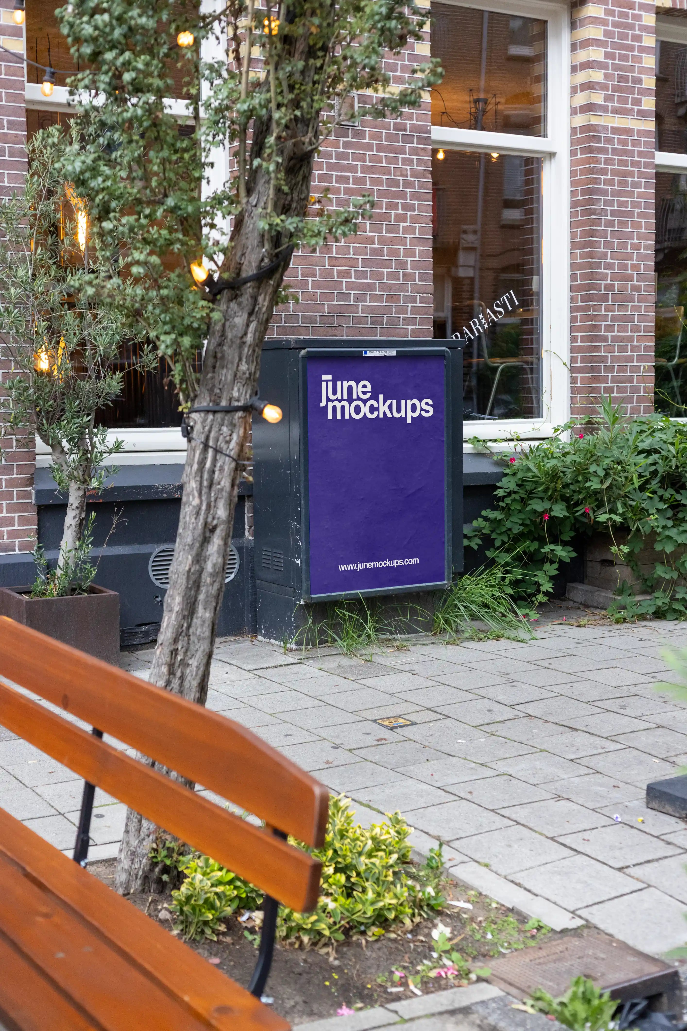 Amsterdam De Pijp poster display mockup in DIN format placed outside a brick café building with trees and urban sidewalk setting in Amsterdam, Netherlands.