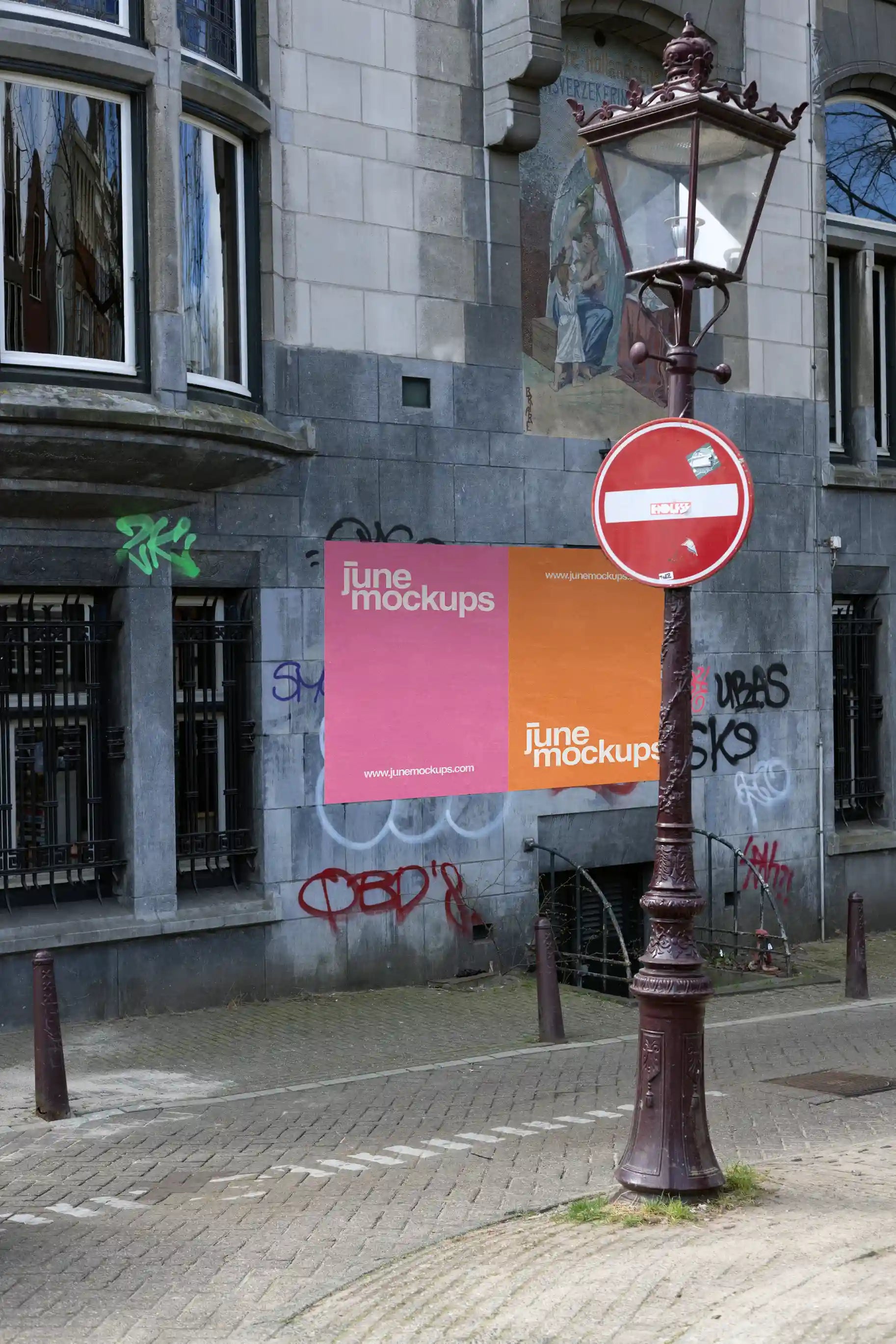 Two large urban posters on a graffiti-covered wall in Amsterdam with a vintage street lamp in front.