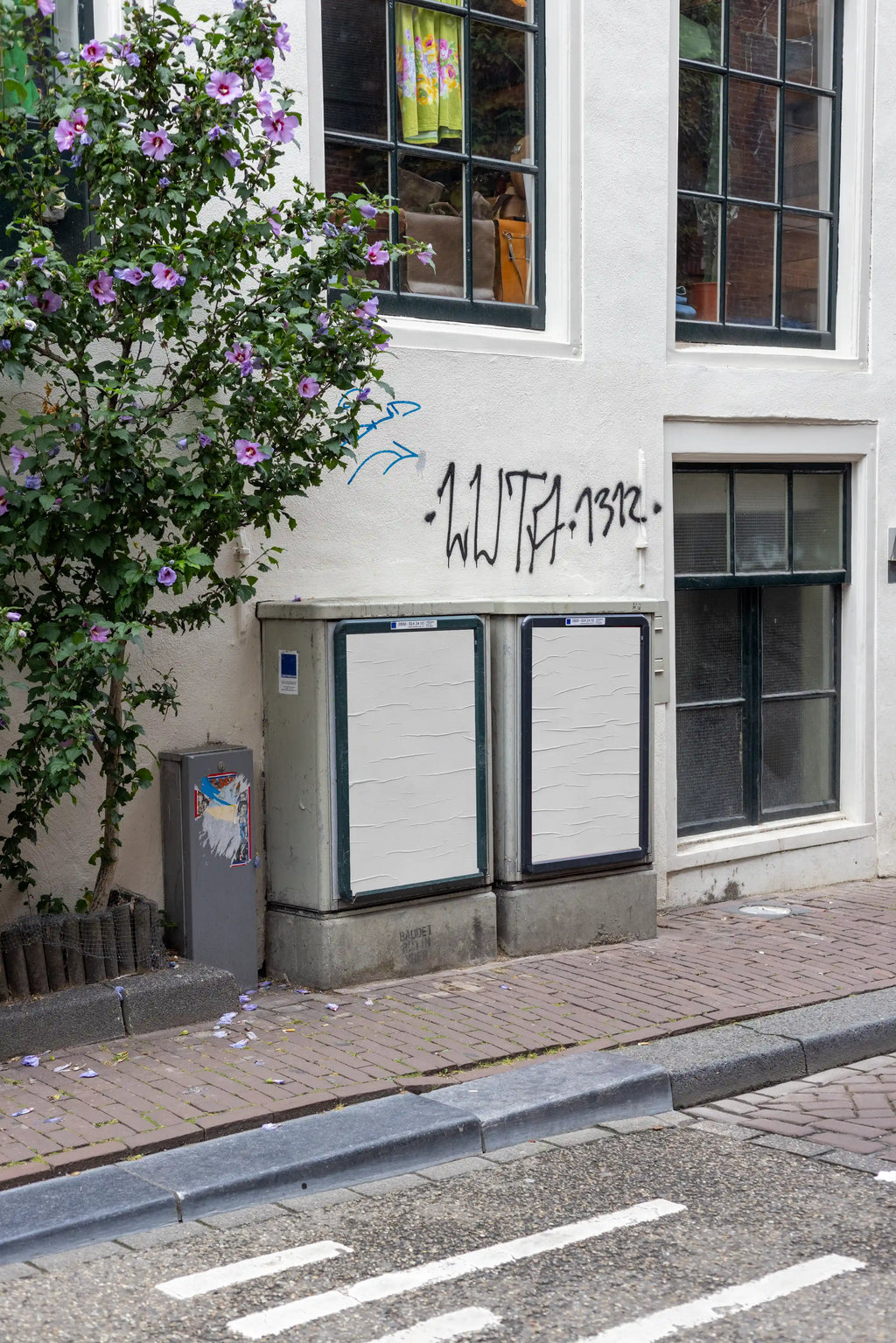 Amsterdam Haarlemmerdijk urban poster mockup featuring two DIN-format blank posters mounted on street utility boxes in a realistic residential neighborhood with brick pavement and graffiti wall.