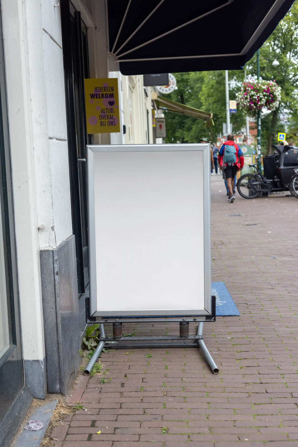 Blank background Amsterdam street A-board poster mockup in DIN format positioned on a sidewalk outside a shop with authentic urban environment and natural daylight.