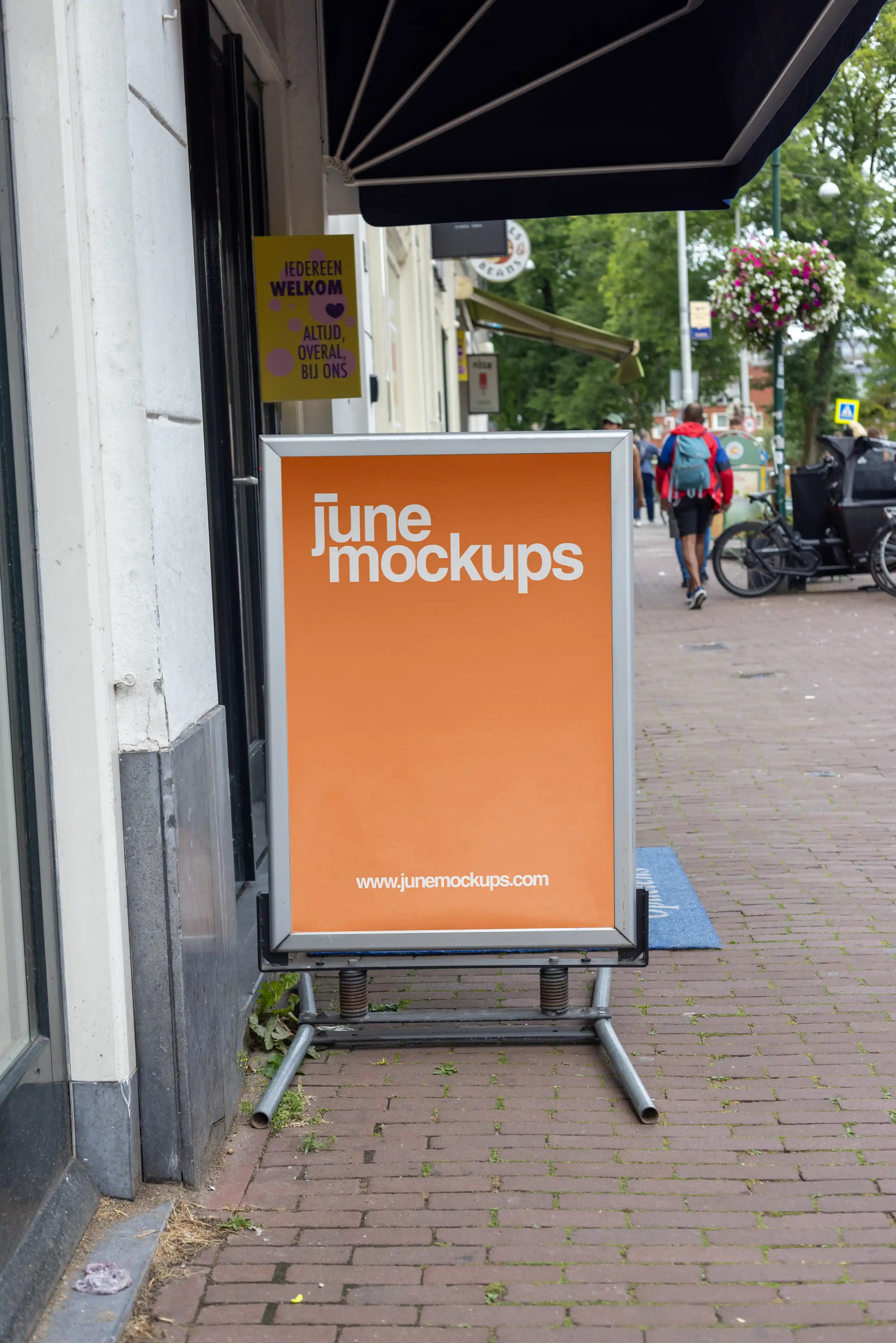 Amsterdam street A-board poster mockup in DIN format placed on a brick sidewalk in front of a local shop with realistic city background, pedestrians, bicycles and storefront details.