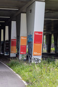 Amsterdam urban poster mockup under a concrete bridge with multiple DIN-format posters placed on large concrete columns surrounded by graffiti, greenery and a realistic city environment.