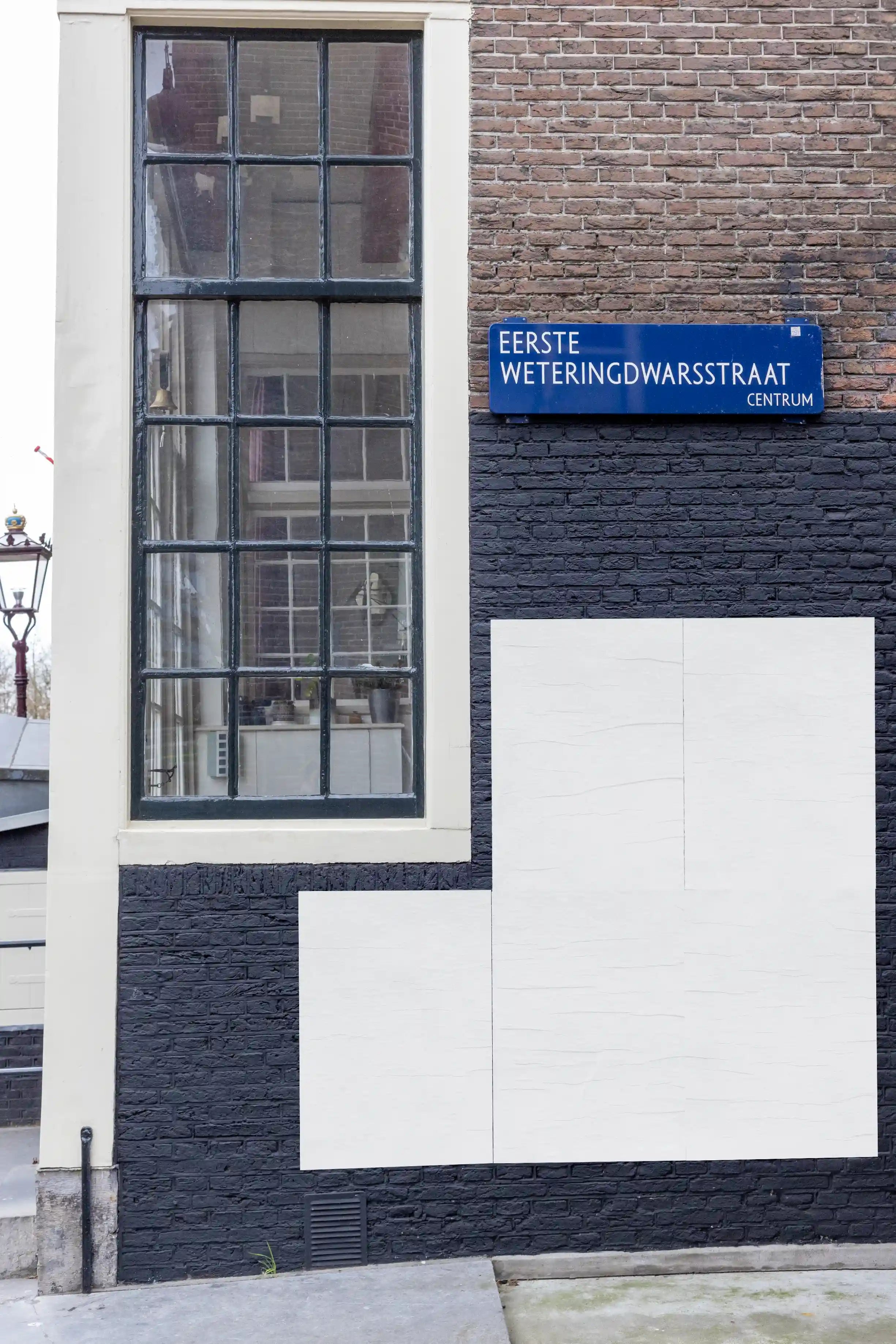 Close-up of an Amsterdam urban street poster mockup on Eerste Weteringdwarsstraat, brick wall with large vintage window.