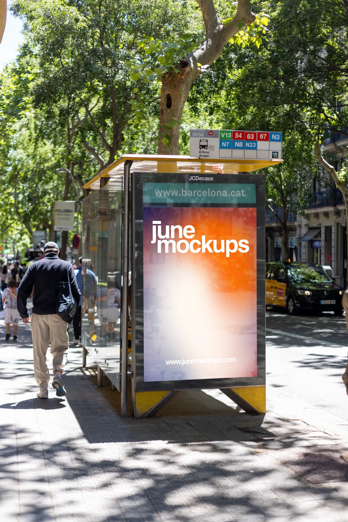Authentic Barcelona bus stop city light mockup photographed at Aribau–Aragó in the Eixample district, featuring a vertical JCDecaux outdoor advertising display with a bright JuneMockups gradient design. The poster is integrated into a glass public transport shelter with a distinctive yellow roof, metal frame and clearly visible bus route information above the advertising panel. A turquoise Barcelona city information strip appears above the poster area, emphasizing the authentic local setting. Tall plane tre