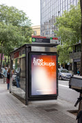 Photorealistic bus shelter poster mockup photographed at the Pau Claris–Mallorca public transport stop in Barcelona's Eixample district, Spain. A vertical JCDecaux advertising panel featuring a colorful JuneMockups design is integrated into a modern glass bus shelter with a brushed metal roof and visible route information signage. The image is captured from a slightly angled street-level perspective, revealing the transparent side panels and natural reflections of the surrounding environment. A contemporary
