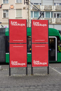 Four red DIN poster mockups on two outdoor advertising stands at Claraplatz in Basel, with a green tram passing in the background. The urban scene includes city buildings, pavement and public transport details, designed for transit advertising, poster campaigns and out-of-home branding presentations.