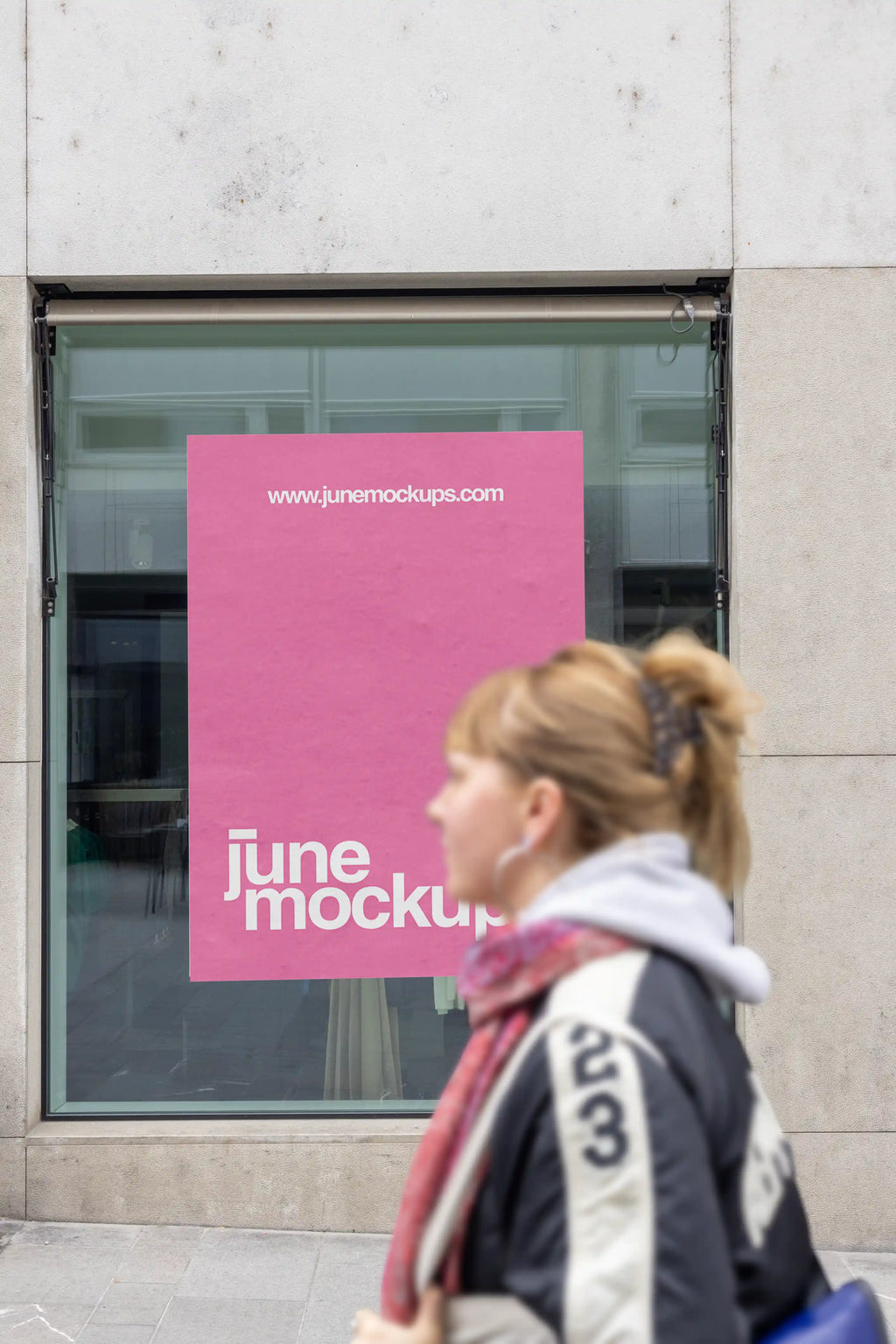 Pink poster mockup displayed inside a shop window on Freie Strasse in Basel, one of the city’s main shopping streets. A blurred person walks past in the foreground, with glass reflections, a modern storefront and clean stone facade around the poster.