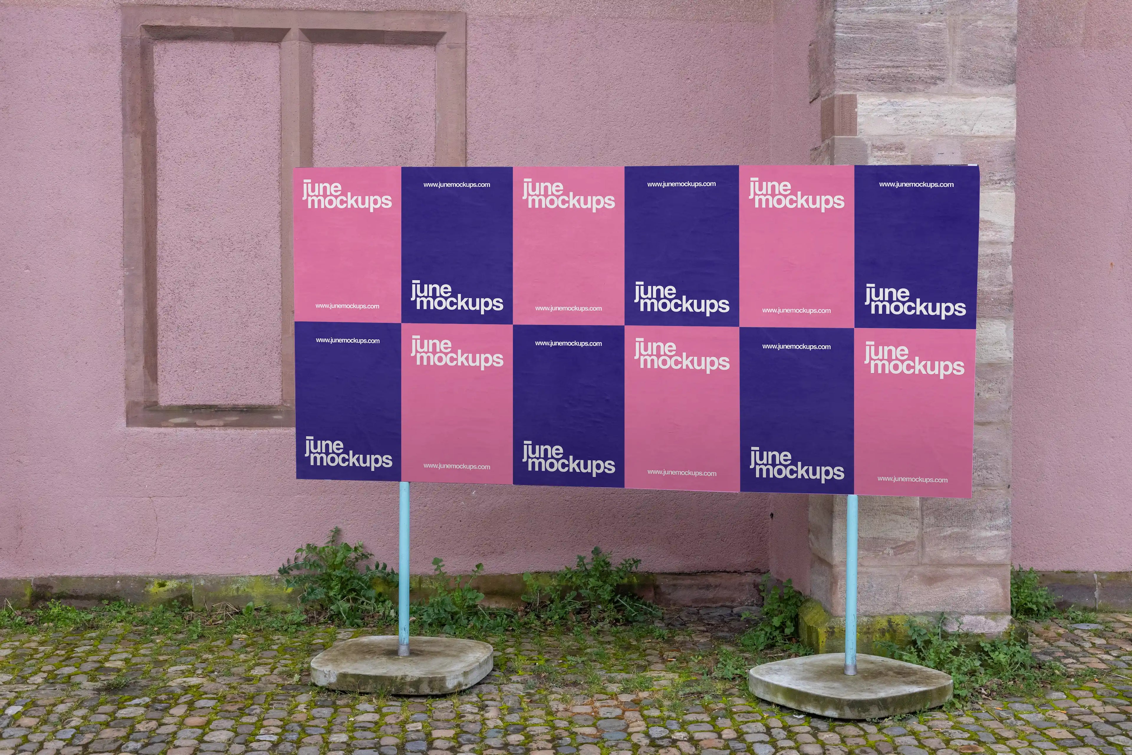 Large outdoor grid poster mockup at Kaserne Basel near Ausstellungsraum Klingental, featuring twelve DIN format poster placements arranged in two rows on a freestanding board. The scene includes a pink textured wall, stone details, cobblestone ground, greenery and natural street surroundings.