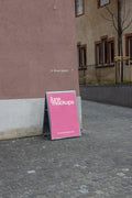 Pink DIN poster mockup attached to a freestanding magnetic board with visible metal corner magnets at Kasernenhof in Basel. The board leans on a cobblestone pathway beside a pink textured wall, with the word Kasernenhof visible in the background.