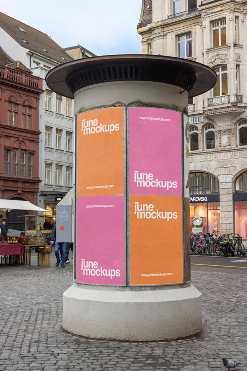 Cylindrical advertising column mockup at Basel Marktplatz with four vertical DIN poster placements in orange and pink. The scene is surrounded by historic buildings, cobblestone pavement, bicycles, market details and a lively city street atmosphere, ideal for Litfaßsäule and ad column poster previews.