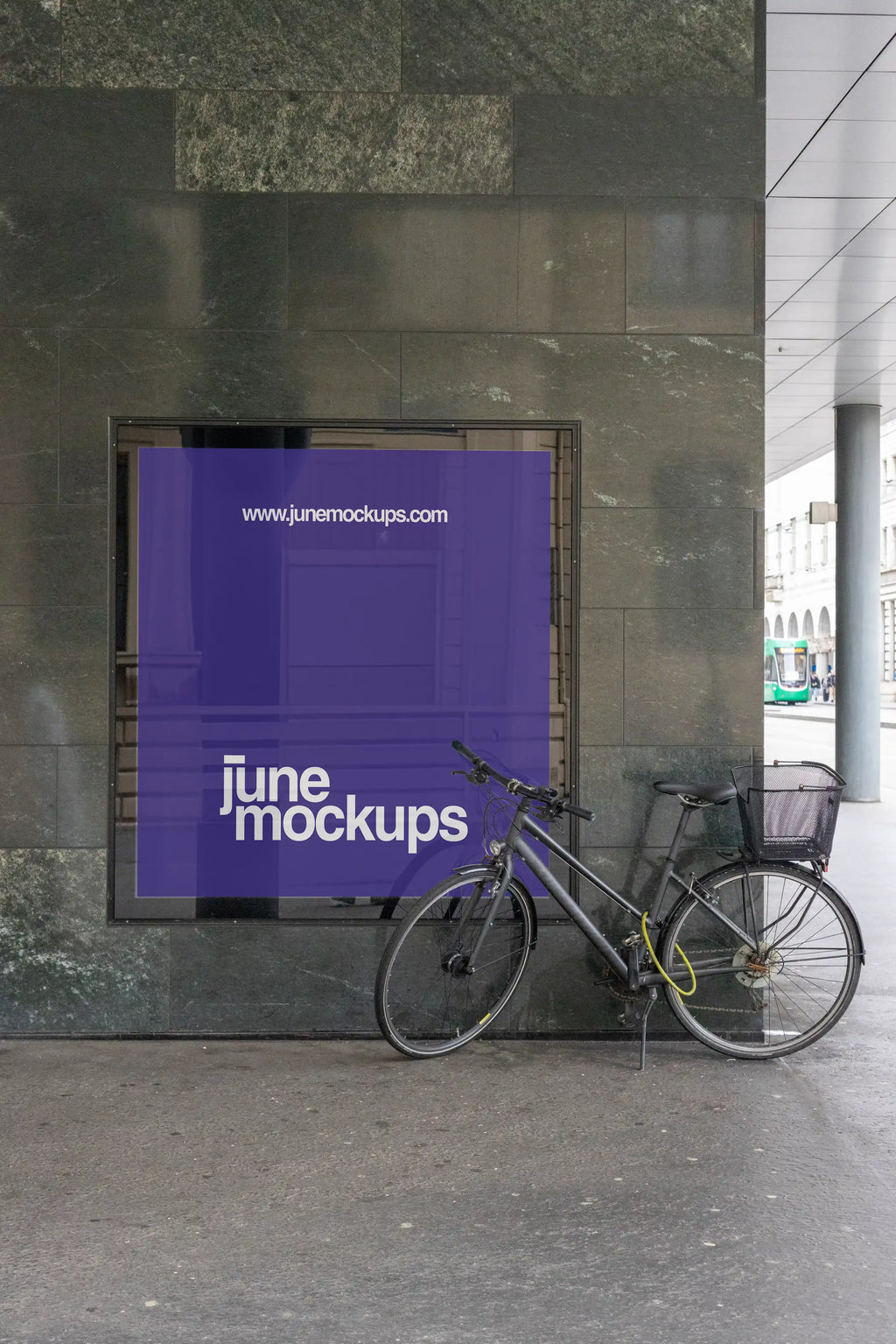 Square purple city light display mockup in Basel set into a dark stone wall, with a bicycle parked in front of the frame. The scene includes reflective glass, polished stone texture, pavement, a covered walkway and a green tram visible in the background.