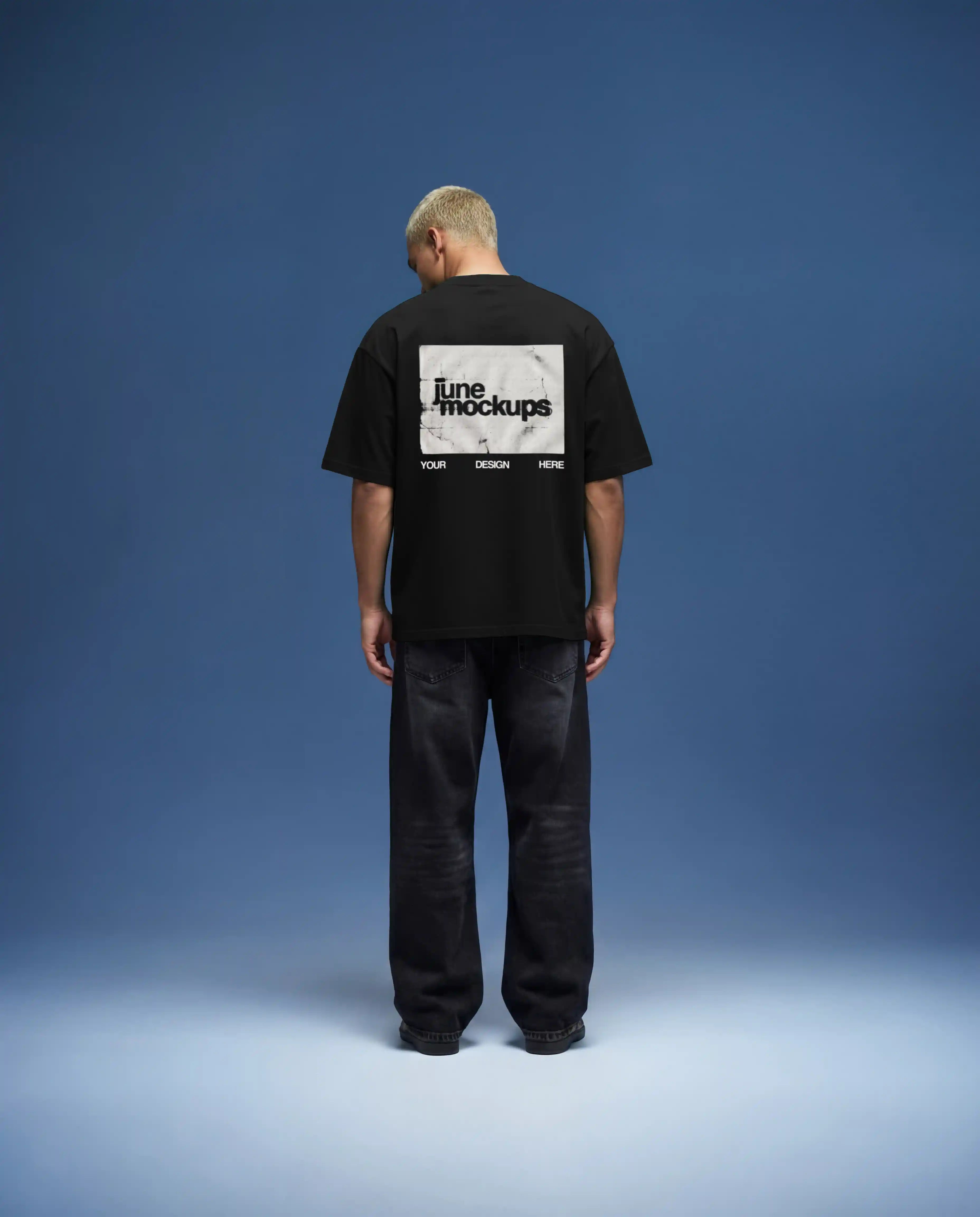 Black oversized t-shirt mockup back view featuring large rectangular back print design, realistic fabric folds and shadows, worn by male model in clean studio environment with soft blue background, high resolution apparel mockup for streetwear branding and graphic design presentation.