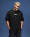 Black oversized t-shirt mockup front close-up with small centered chest logo, detailed cotton fabric texture, natural wrinkles and soft shadows, studio lighting on blue background, perfect for logo branding, minimalist apparel design and high resolution mockup use.