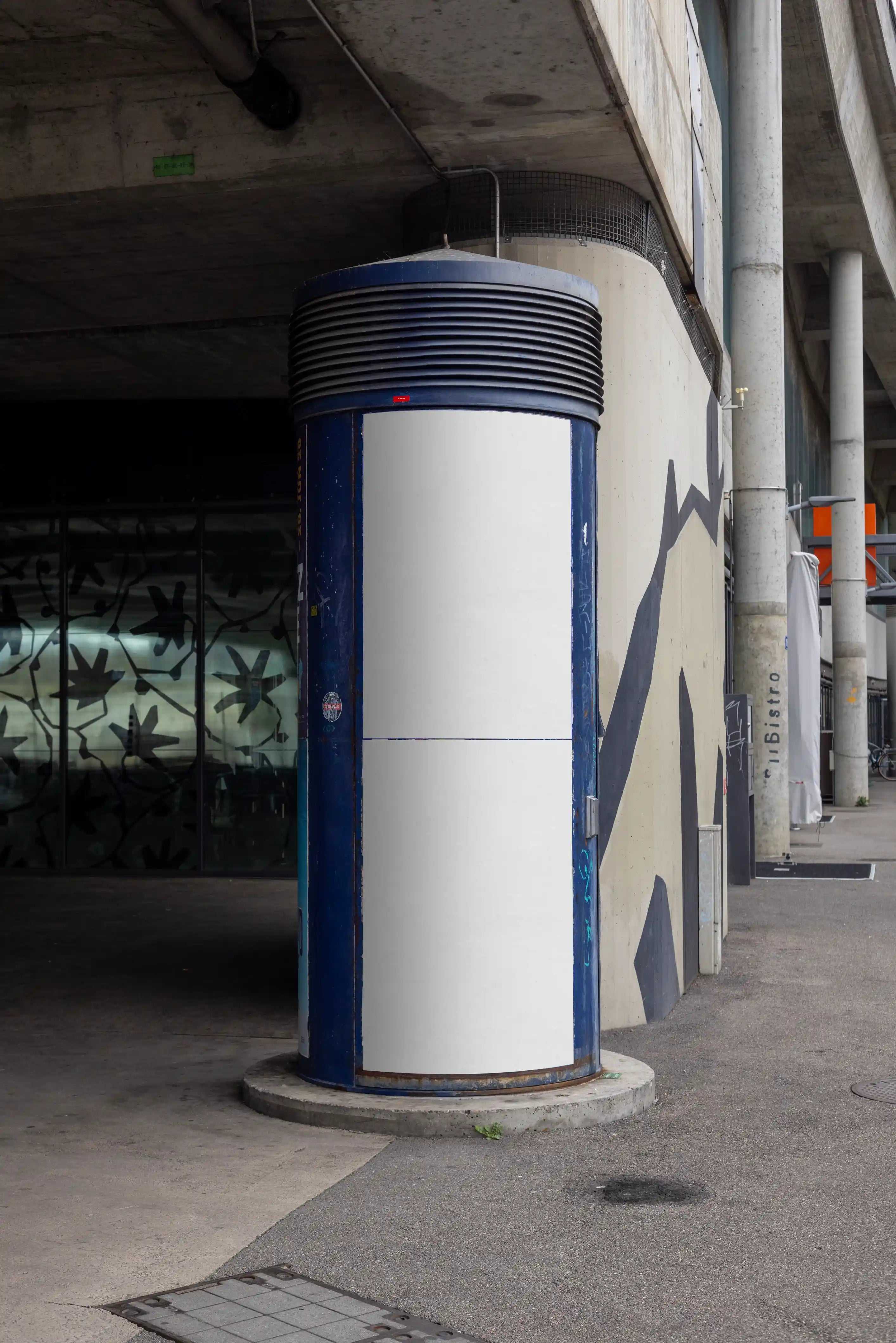 Blank white two-part poster mockup on a curved blue advertising column in Basel under a concrete bridge structure. The urban setting includes worn surfaces, shadows, concrete architecture and street surroundings, ideal for Litfaßsäule mockups, DIN poster previews and outdoor advertising concepts.