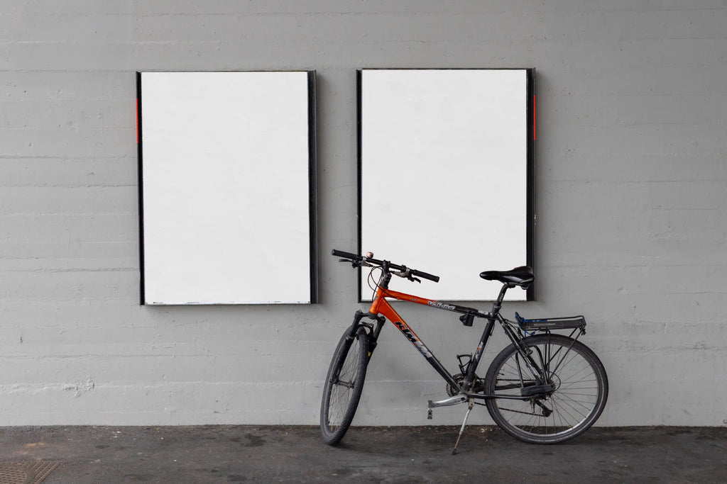 Two blank white DIN poster mockups on a grey concrete wall under a bridge in Basel, with black poster frames and a bicycle leaning in front of the right display. The scene includes realistic paper texture, subtle wall stains, pavement marks and an authentic urban street setting.