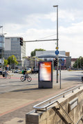 Outdoor city light poster mockup at Aegidientorplatz, Hanover. Captures a lively street scene with cyclists and urban architecture. Ideal for showing realistic campaign visuals or transportation-related designs.