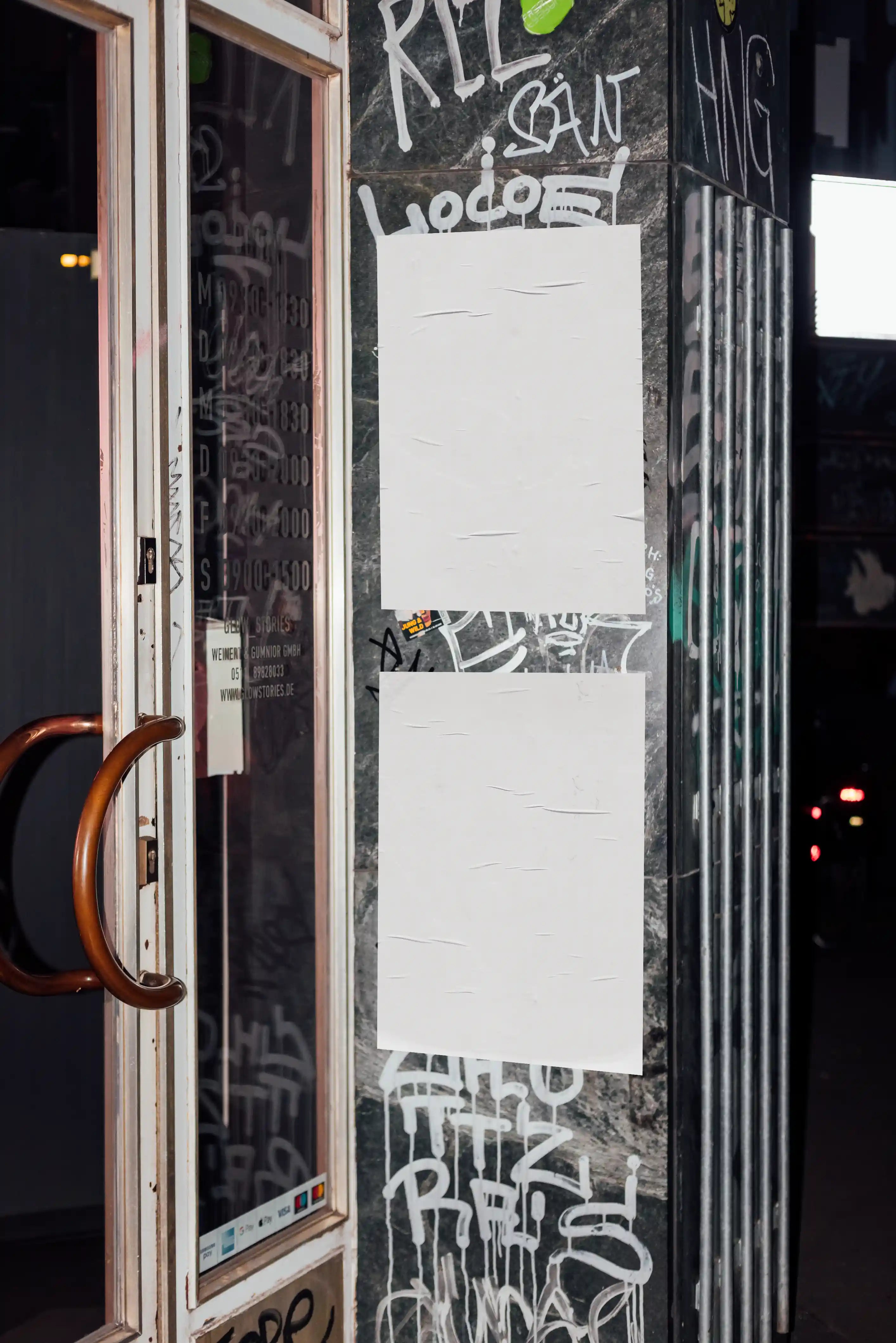 Urban poster mockup with blank posters on a graffiti-covered street wall next to a door, ideal for showcasing designs in a realistic outdoor advertising environment.