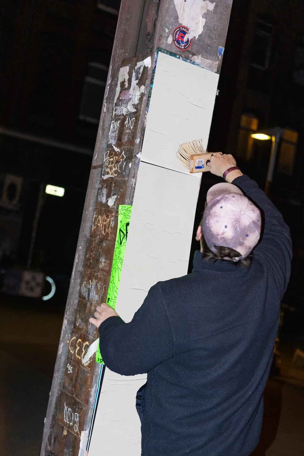 Urban poster mockup with blank posters being applied on a street pole at night, perfect for realistic outdoor advertising presentations and branding.
