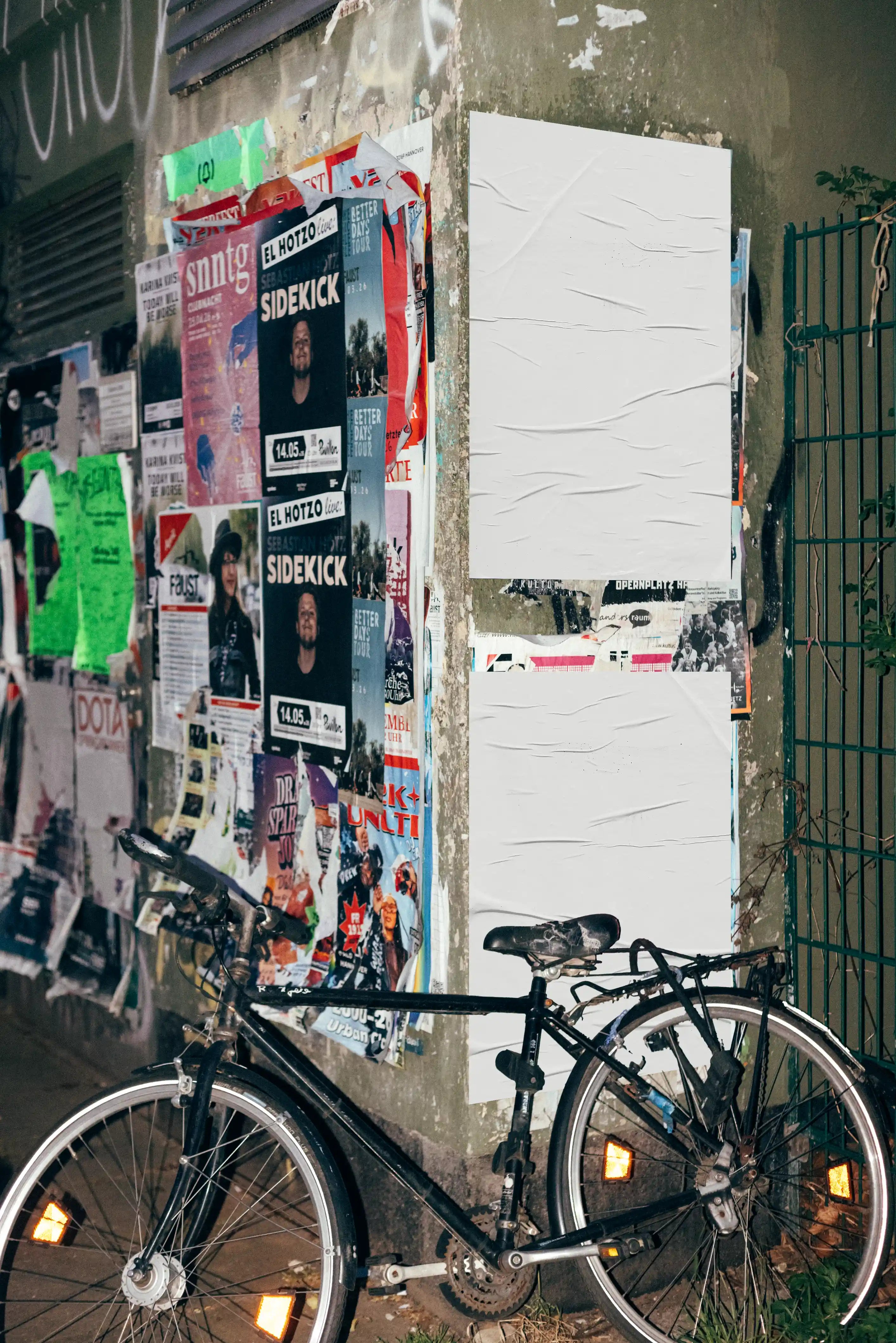 Urban poster mockup with blank posters placed on a grunge street wall with layered posters and a bicycle in the foreground, ideal for showcasing designs in a realistic outdoor advertising environment.