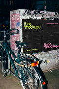 Urban poster mockup at night featuring street posters on a grunge wall next to a bicycle, capturing a realistic city advertising scene with authentic lighting and textures.
